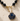 Necklace with black beads and a blue and gold shell pendant on a beige background