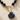 Necklace with black beads and a blue and gold shell pendant on a beige background