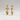 A pair of gold dangle earrings with three stacked oval and round beads on each earring, displayed against a neutral light gray background.