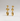 A pair of gold dangle earrings with three stacked oval and round beads on each earring, displayed against a neutral light gray background.